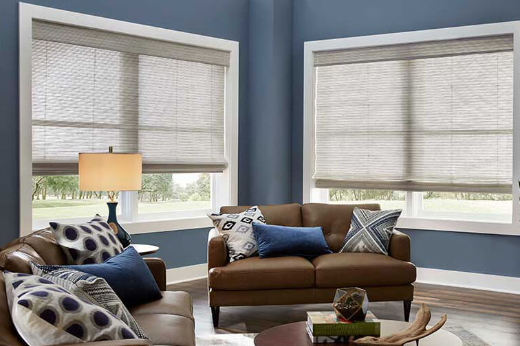 A blue living room with two big windows half-covered by white shades made with natural materials.
